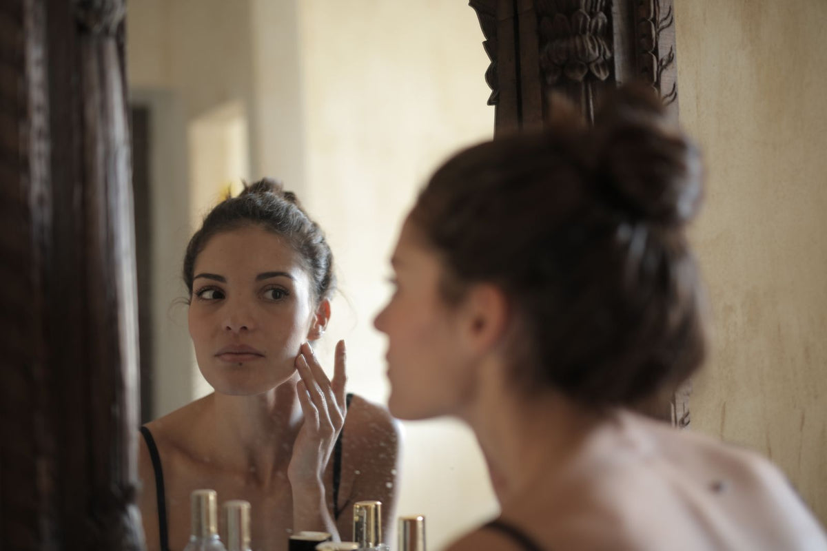 Kvinde rører ved kinden og ser sig selv i spejlet – Ozempic face og hud efter vægttab – Trondahl Skincare
